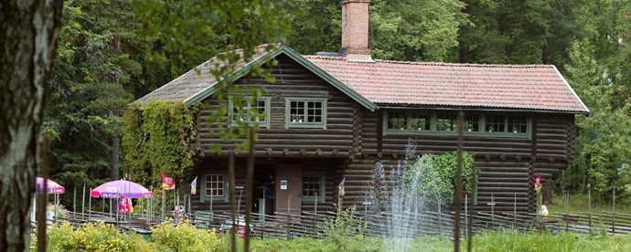 Bild som visar timmerhus framför en damm