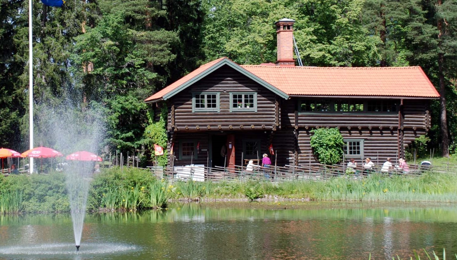 Bild som visar timmerhus framför en damm