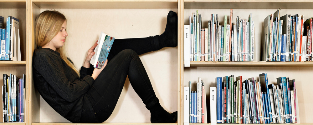 Flicka sitter i bokhylla omgiven av böcker