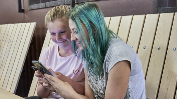 Två ungdomar sitter bredvid varandra, ler och kollar på en telefon.