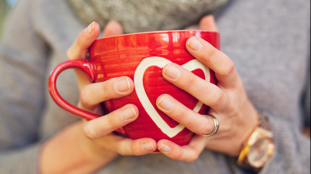 Händer håller i röd mugg med hjärta på. Foto. 