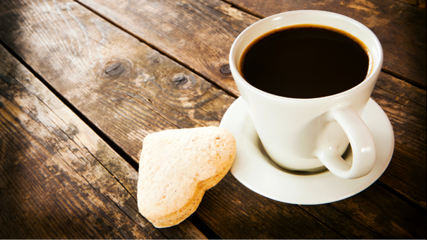 Kaffekopp  och hjärtformad kaka på ett träbord. Foto. 