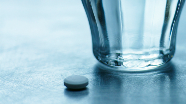 Vattenglas och tablett på bord. Foto.